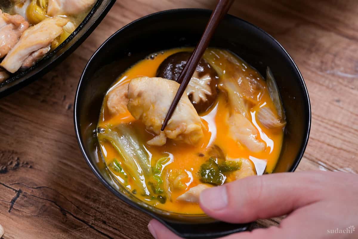 Dipping chicken from chicken sukiyaki in a bowl of whisked raw egg