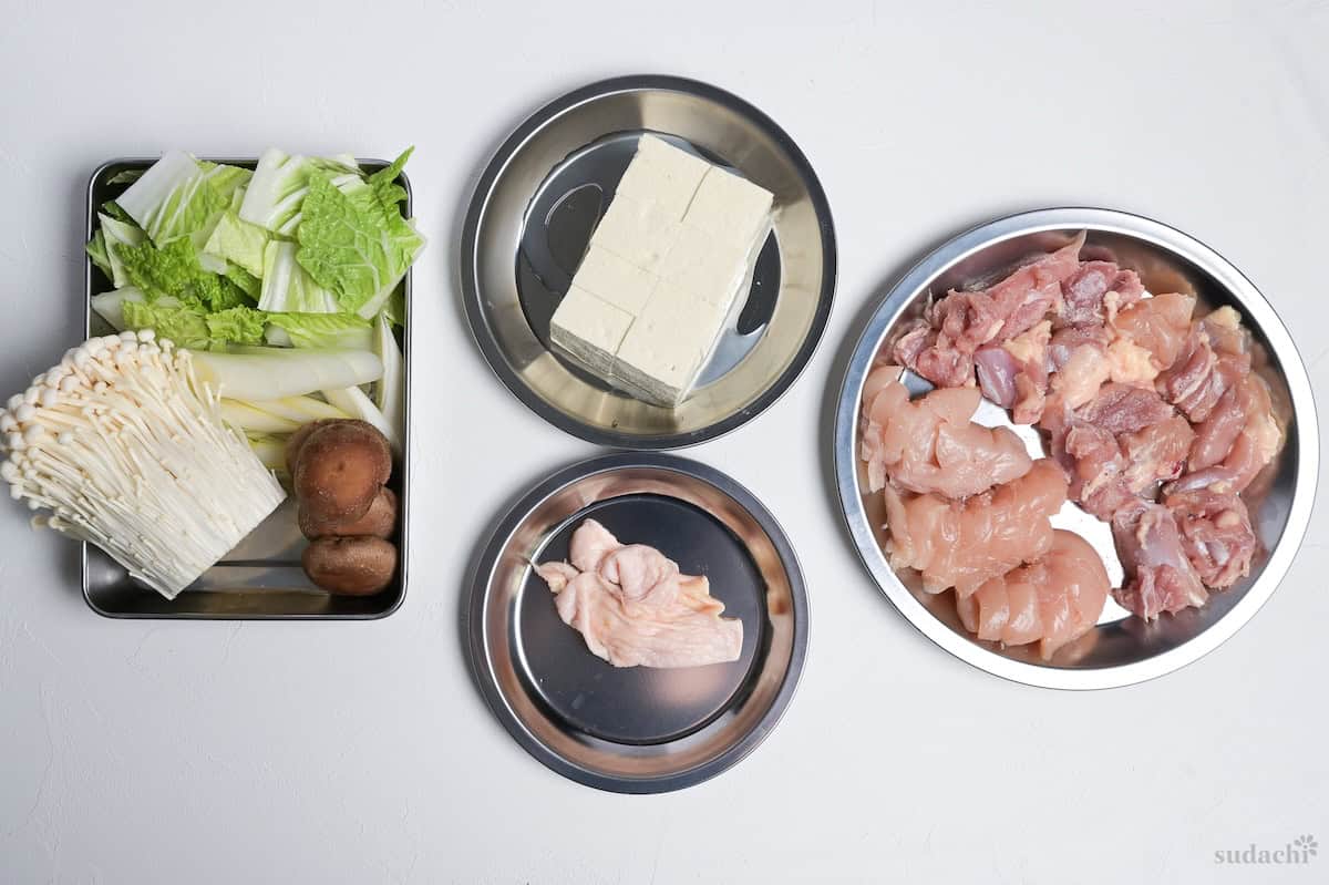 Ingredients to make chicken sukiyaki prepped and placed on silver prep plates