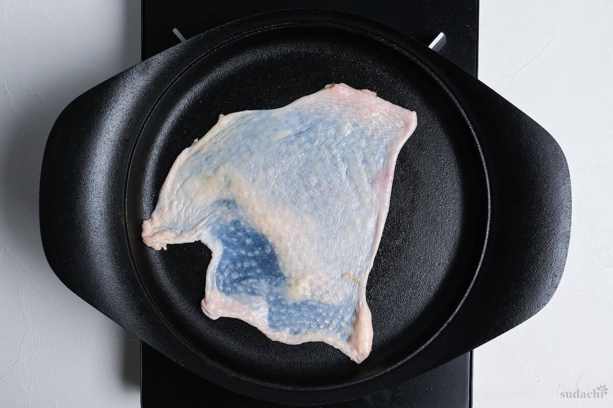 chicken skin spread flat on a cast iron pan on the stove top