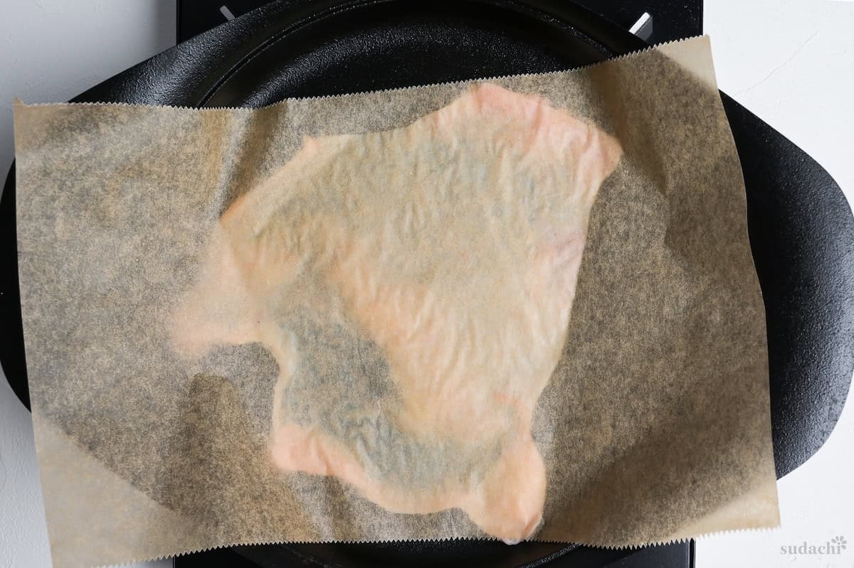 chicken skin with parchment paper on top in a cast iron pan on the stove top