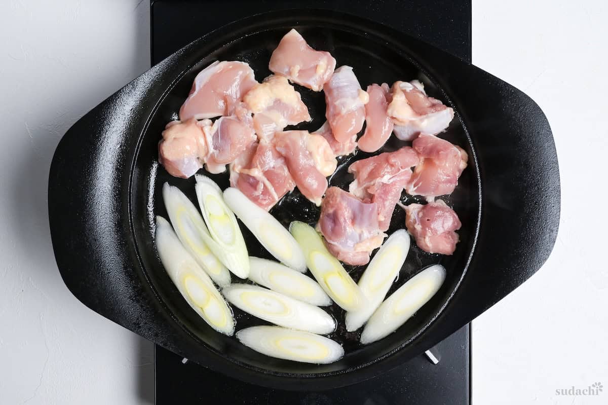 searing chicken thigh and diagonally sliced Japanese leek in a cast iron pot on the stove top