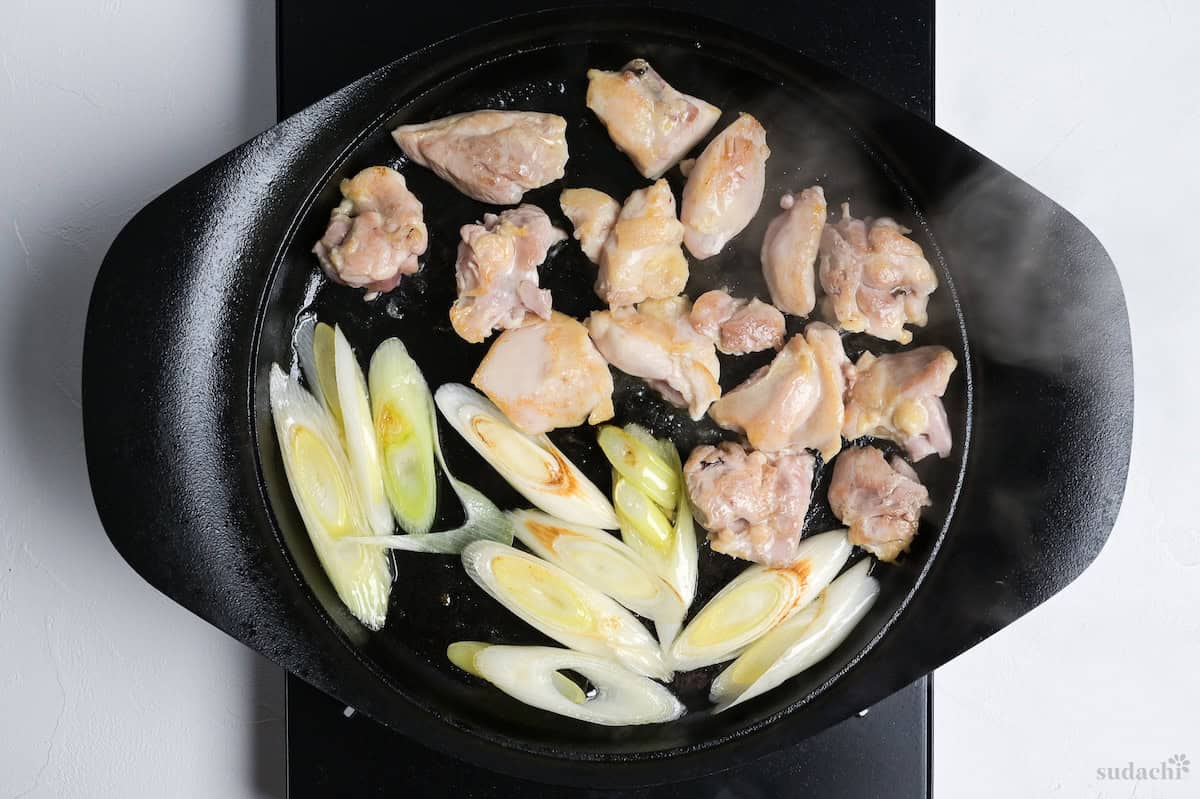 seared chicken thigh pieces and diagonally sliced Japanese leek in a cast iron pot on the stove top