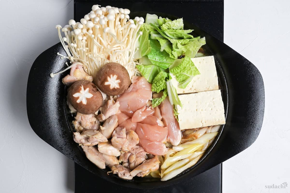 Meat, vegetaboes, and tofu in a cast iron pot with sauce to make chicken sukiyaki
