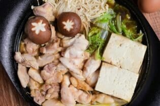 Chicken sukiyaki with enoki mushrooms, shiitake, cabbage and tofu in a cast iron pot, top down view
