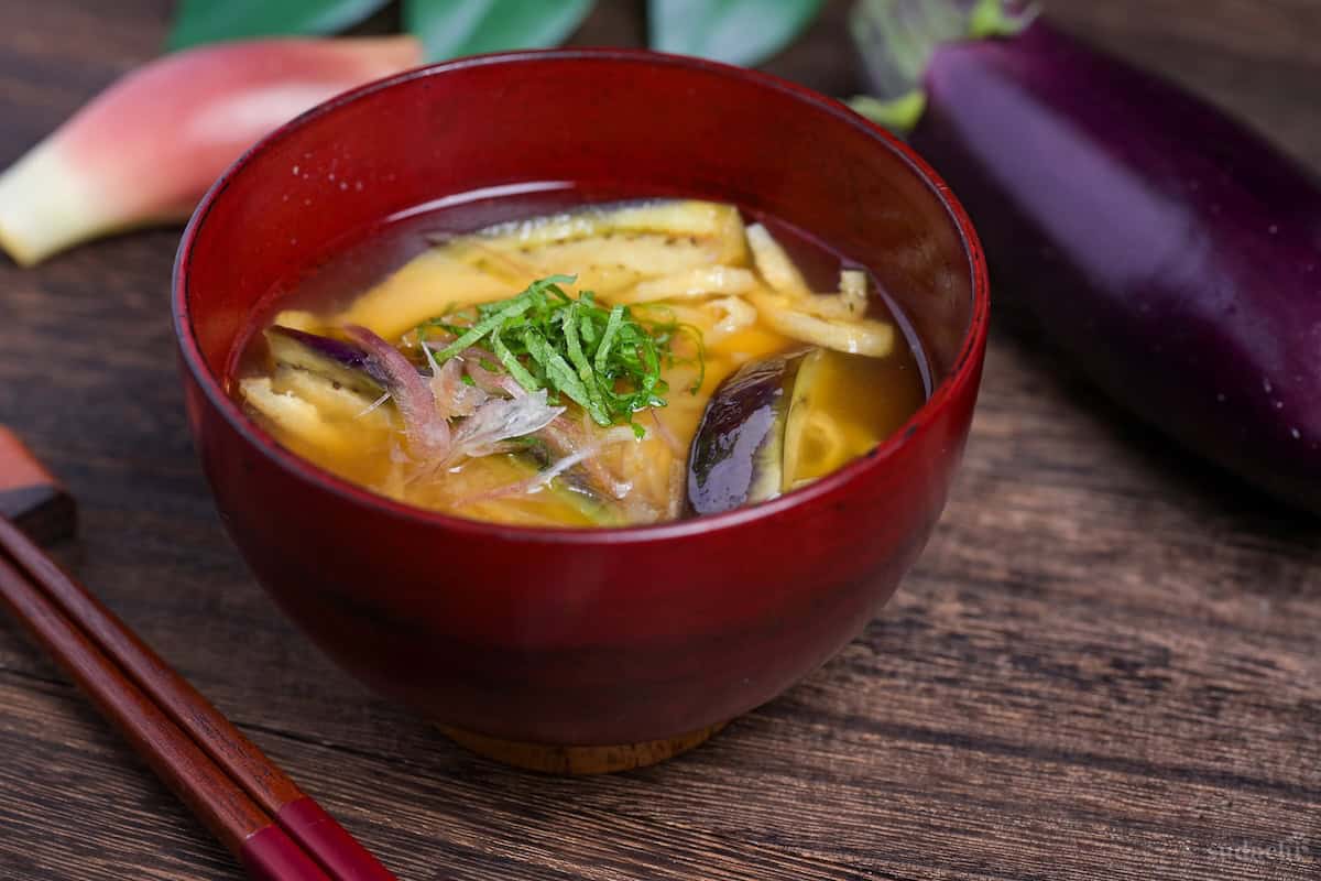 eggplant miso soup topped with Japanese ginger and shredded Perilla leaves in a red bowl side view