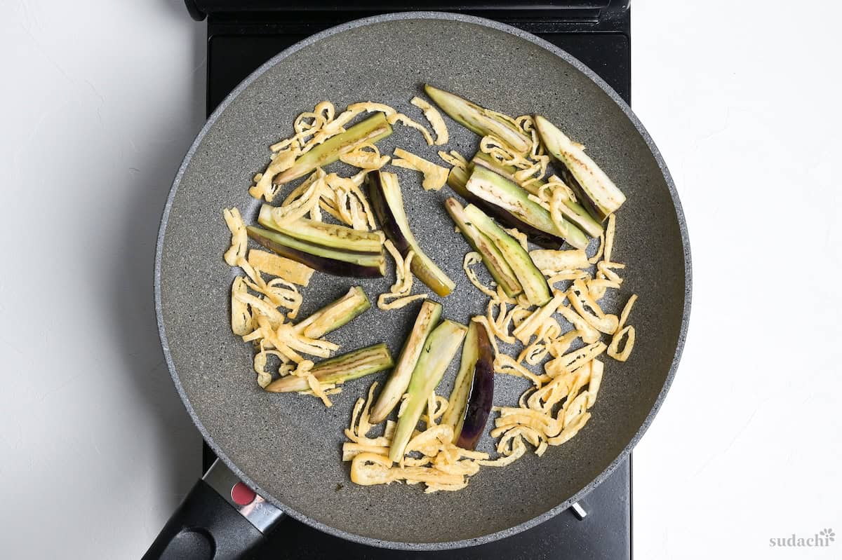 sliced eggplant and tofu pouches seared in a frying pan on the stove top