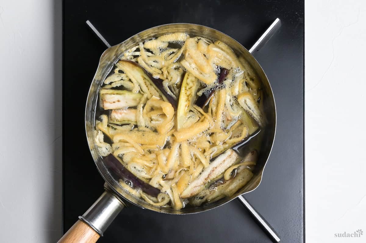 seared eggplant and shredded tofu pouches simmering in dashi broth in a pot on the stove top