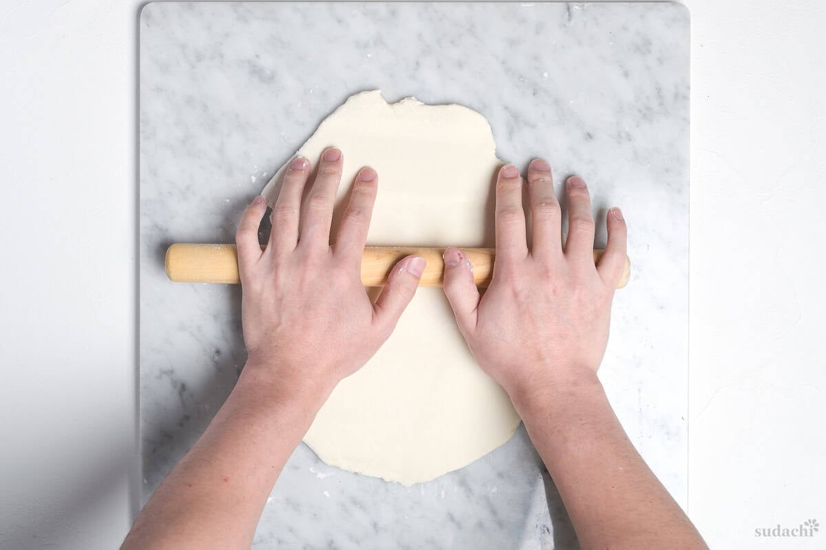 rolling gyoza wrapper dough flat with a wooden rolling pin on a marble kneading board