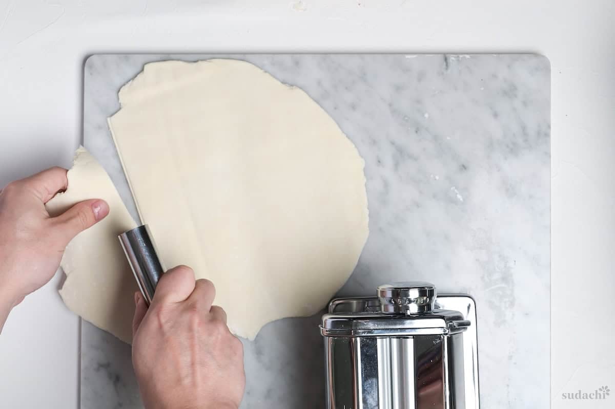 cutting rolled gyoza skin dough into pieces on a marble kneading board