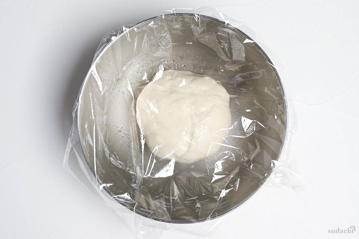 gyoza wrapper dough resting in a bowl covered with plastic wrap
