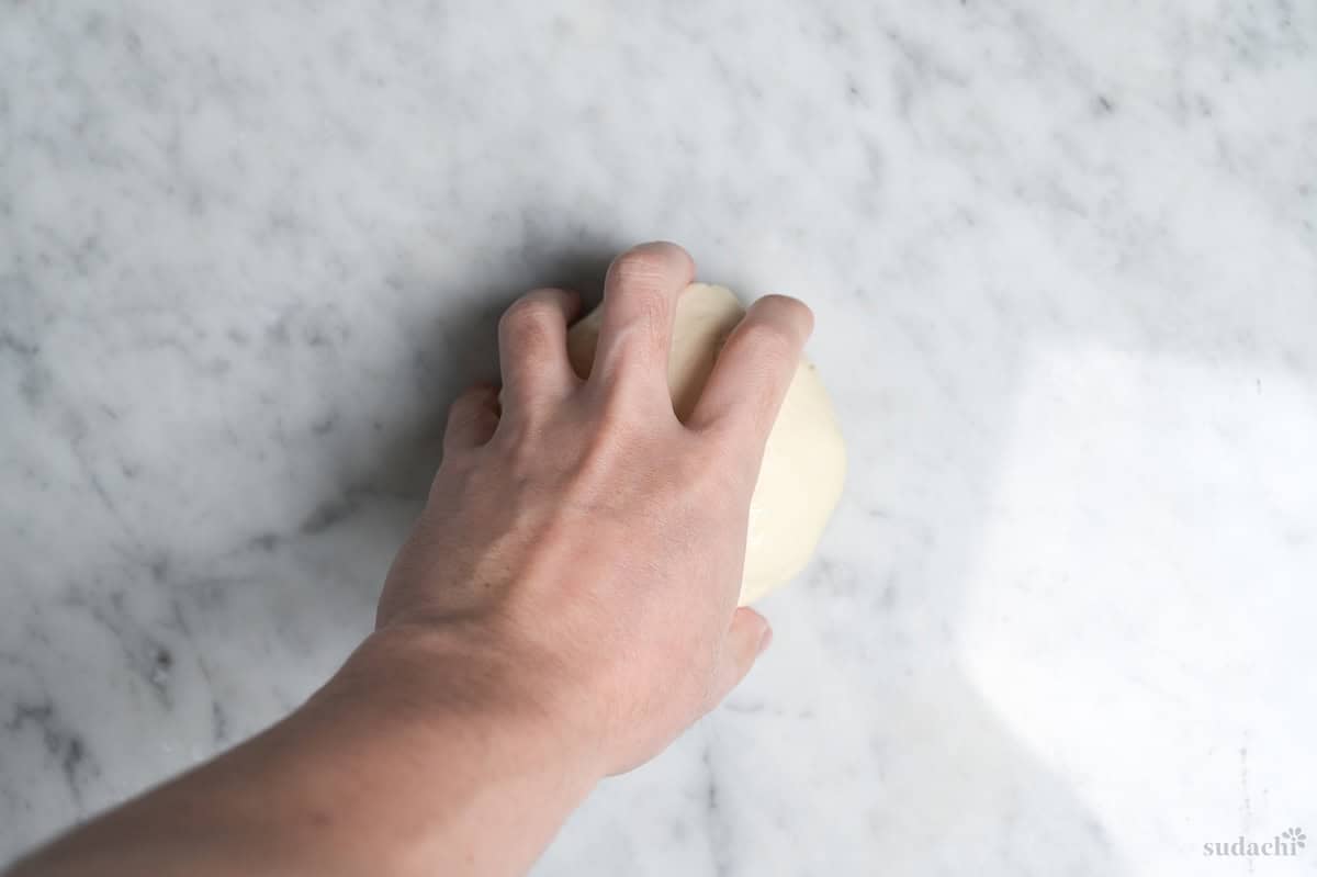 a hand holding gyoza skin dough on a marble kneading board