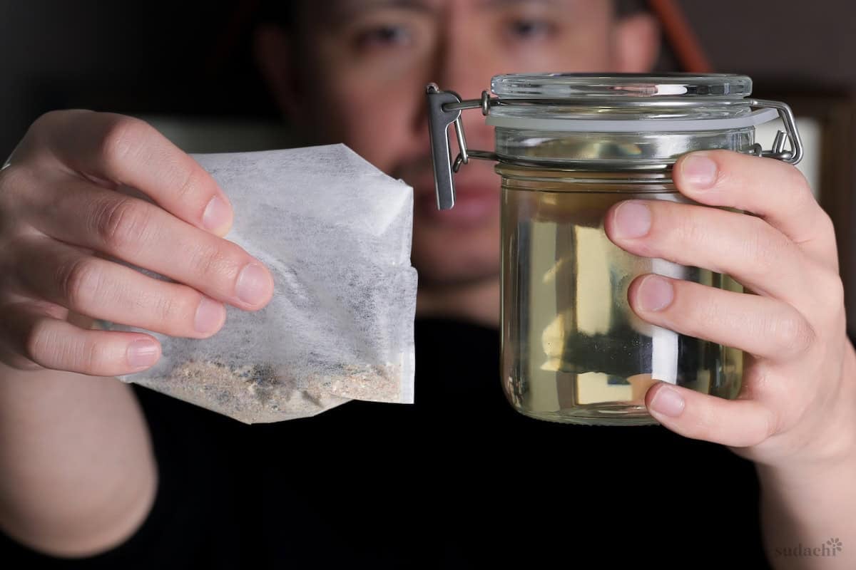 Yuto Omura holding a homemade dashi packet in one hand and a glass jar of brewed dashi in the other