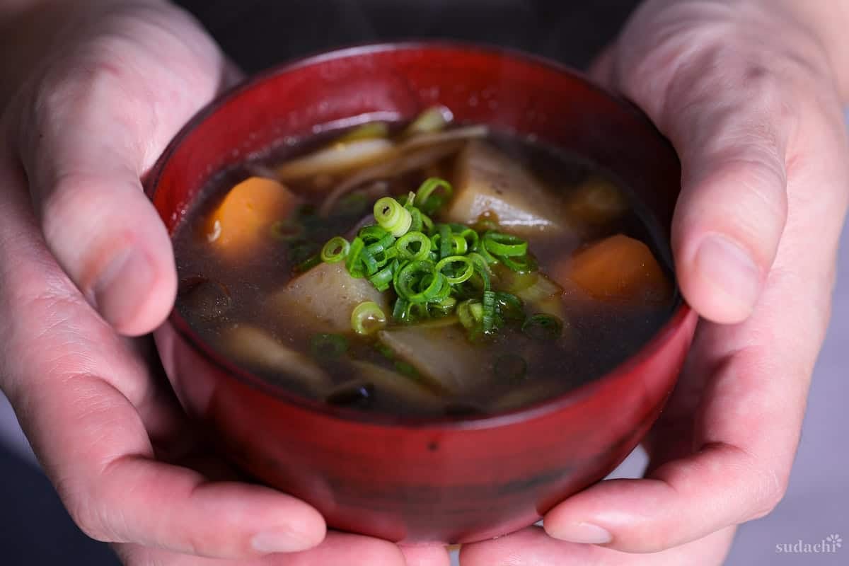 Yuto Omura holding up a bowl of kenchinjiru soup topped with chopped green onions in a red bowl
