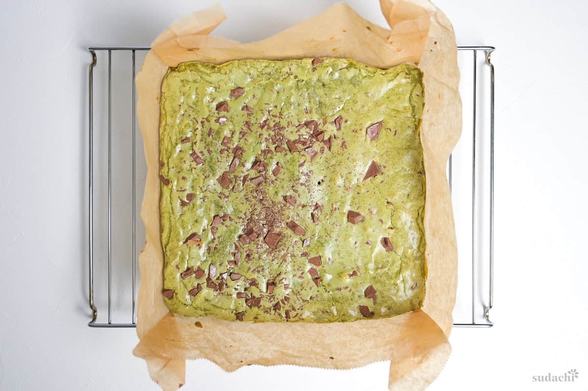 Baked matcha blondie with baking paper on a wire rack to cool