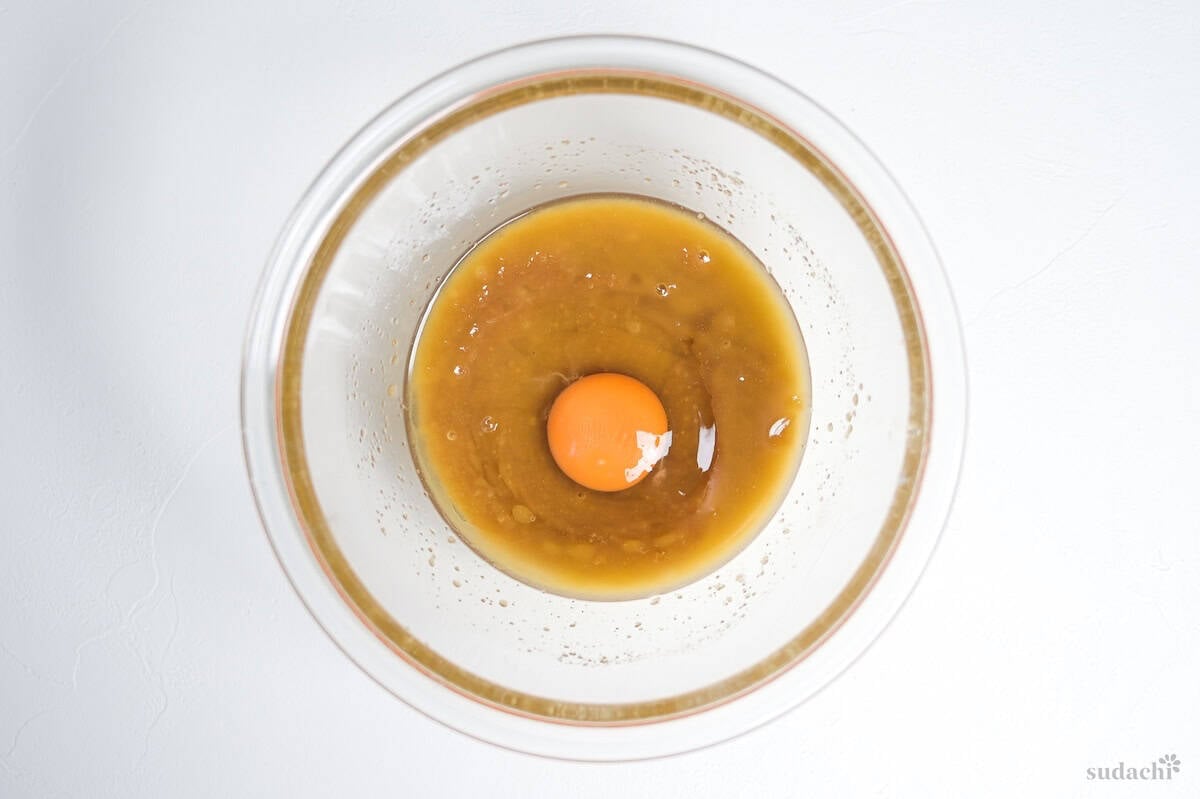 An egg cracked into a bowl with sugar and melted butter