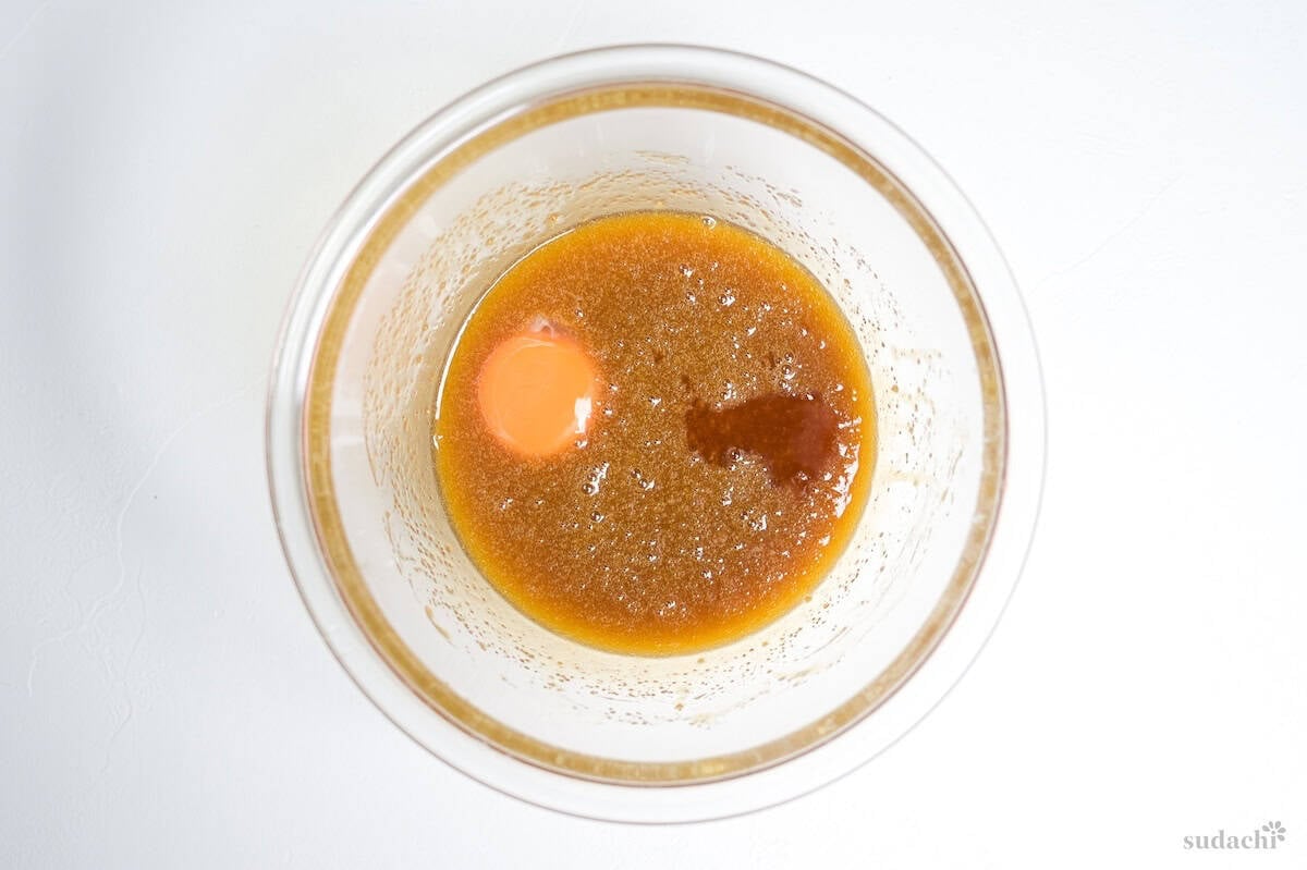 egg yolk and vanilla added to egg, melted butter and sugar mixture in a glass mixing bowl