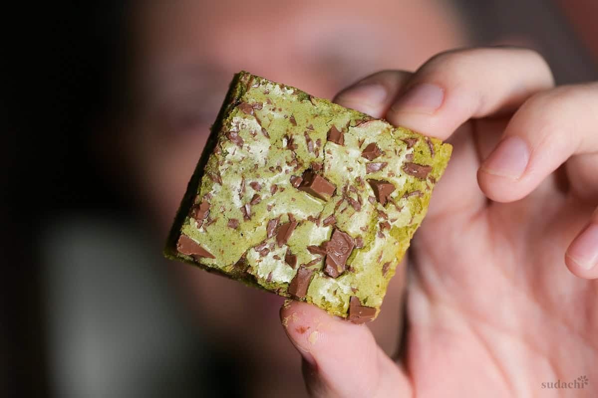 Yuto Omura holding up a matcha blondie topped with chunks of roughly chopped chocolate