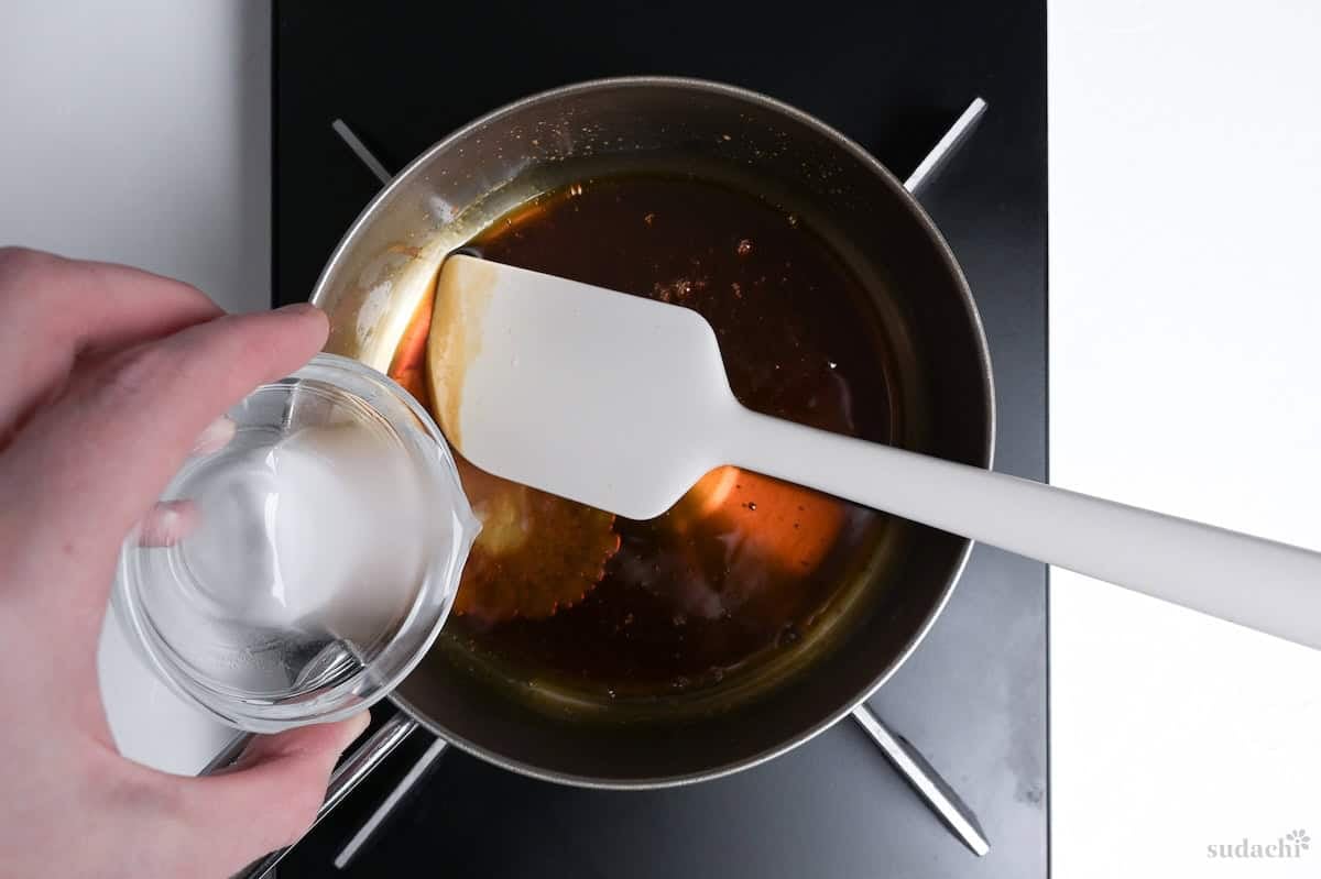 pouring slurry into mitarashi sauce in a saucepan on the stove top
