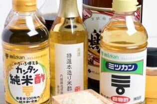 Various brands of Japanese rice vinegar with a wooden masu filled with rice at the front