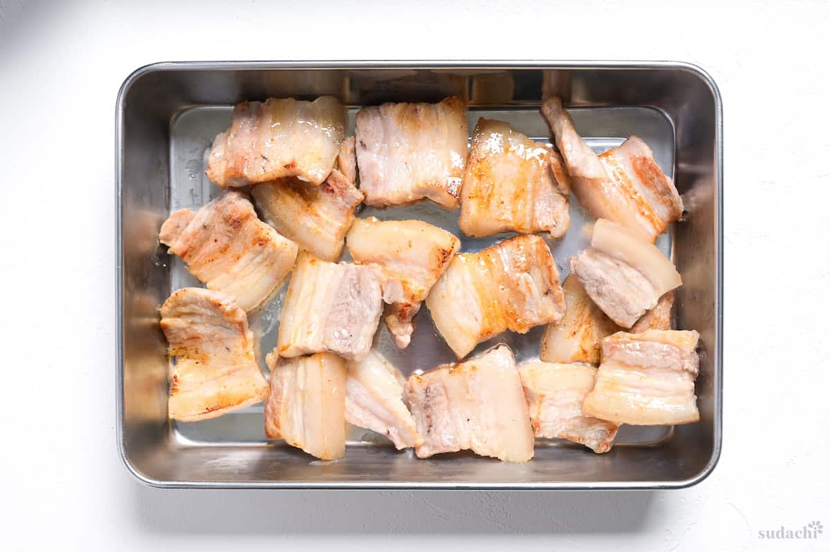 Seared pork belly slices in a metal container.