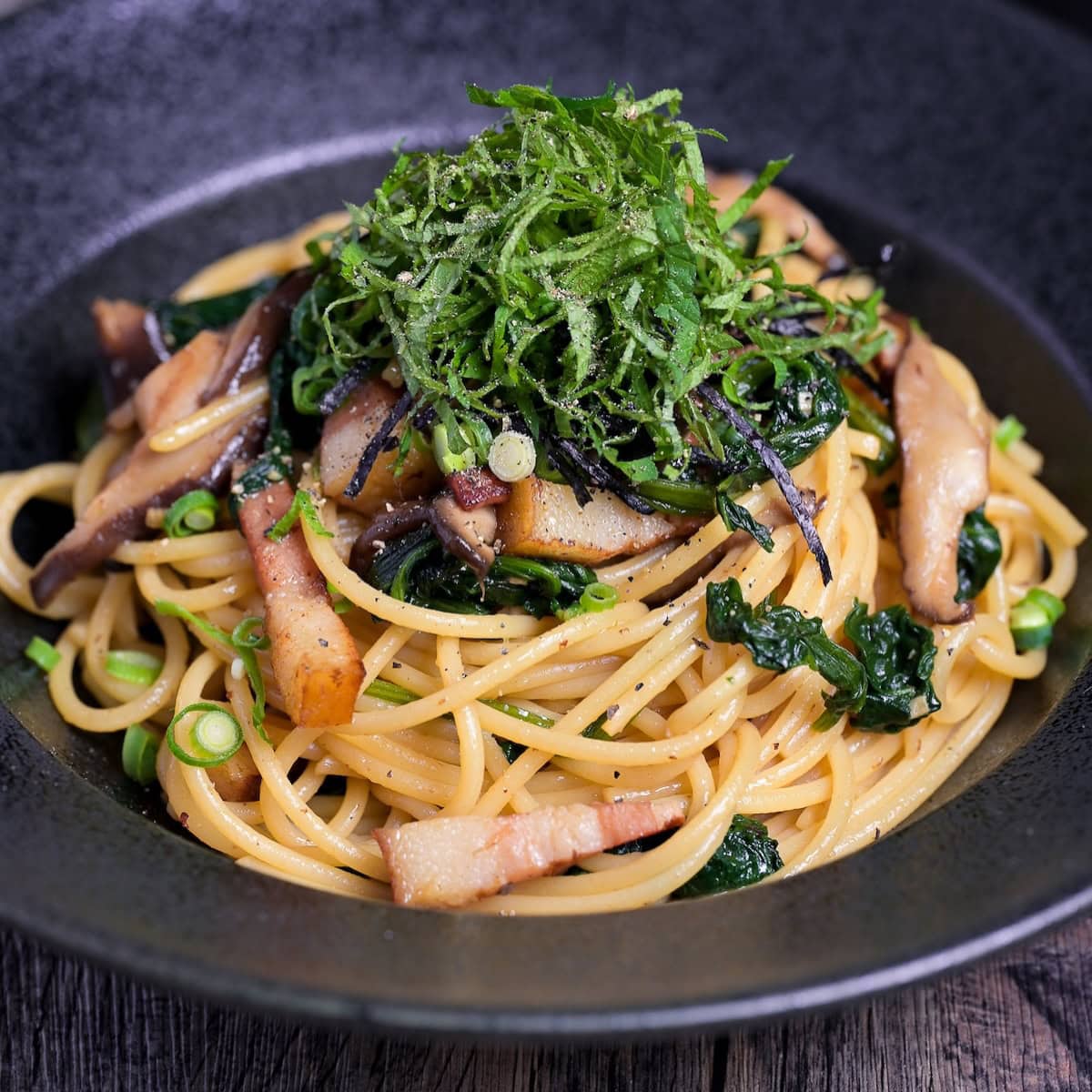 Japanese bacon and mushroom shoyu butter wafu pasta topped with shredded shiso leaves and nori served in a black pasta dish thumbnail