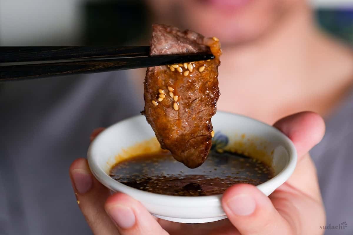 Yuto Omura holding up a piece of beef over a small bowl of homemade yakiniku sauce