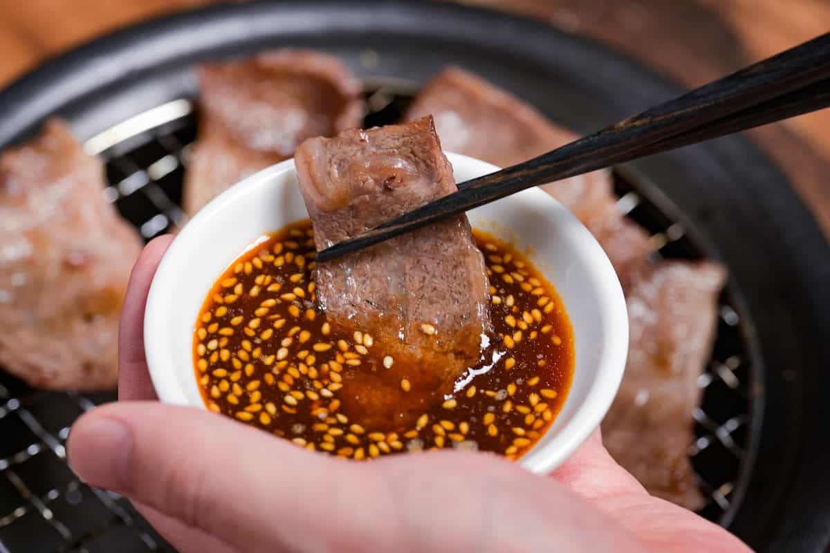 dipping a piece of thinly sliced grilled beef in a bowl of homemade yakiniku sauce