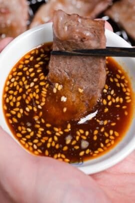 dipping a piece of thinly sliced grilled beef in a bowl of homemade yakiniku sauce