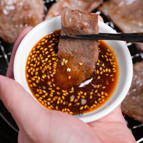 dipping a piece of thinly sliced grilled beef in a bowl of homemade yakiniku sauce