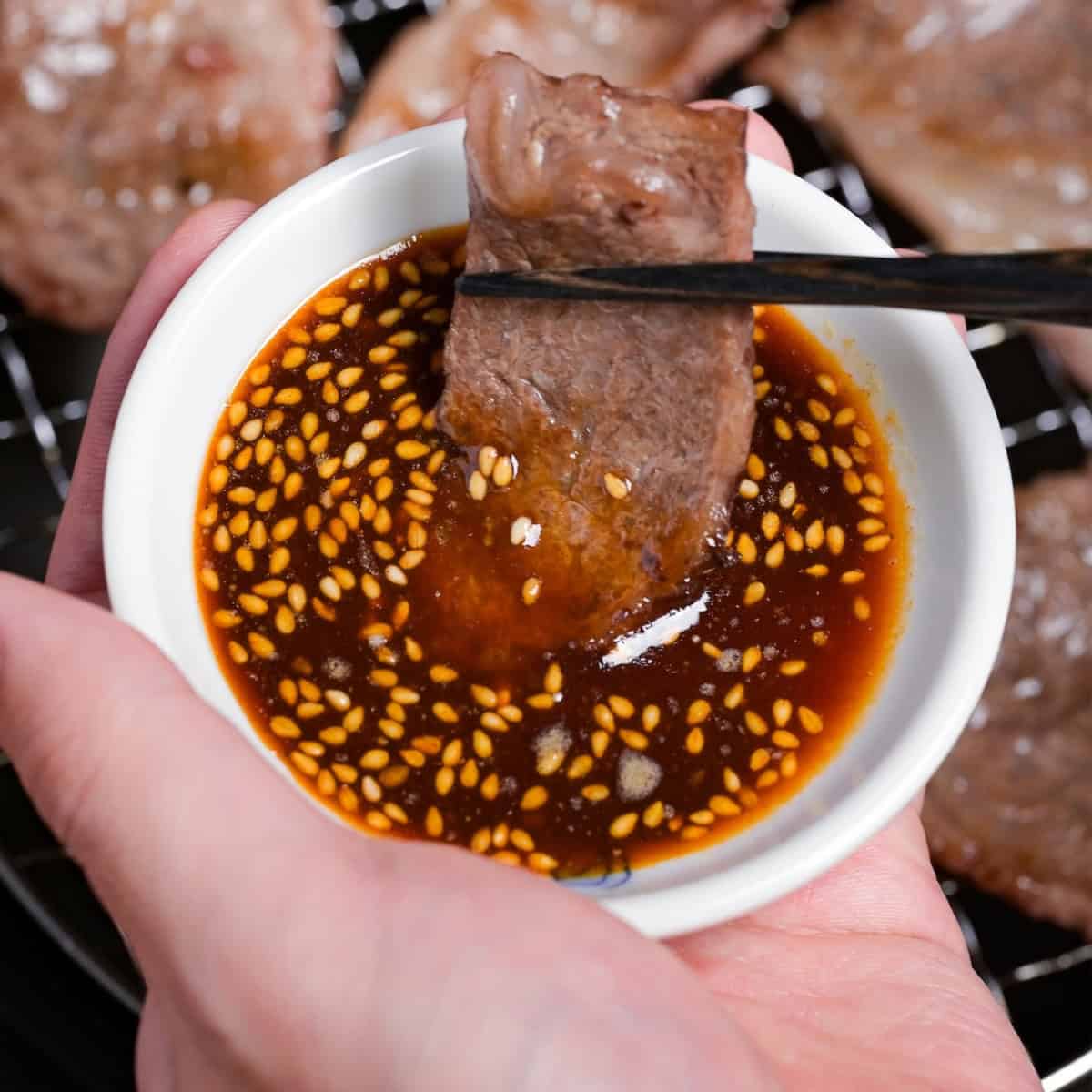 dipping a piece of thinly sliced grilled beef in a bowl of homemade yakiniku sauce