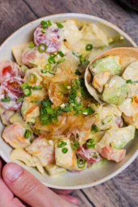 Avocado egg salad in an off-white bowl being scooped up with a light wooden spoon