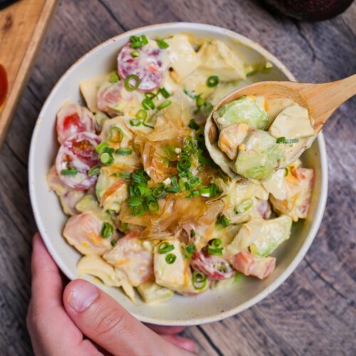 Avocado egg salad in an off-white bowl being scooped up with a light wooden spoon