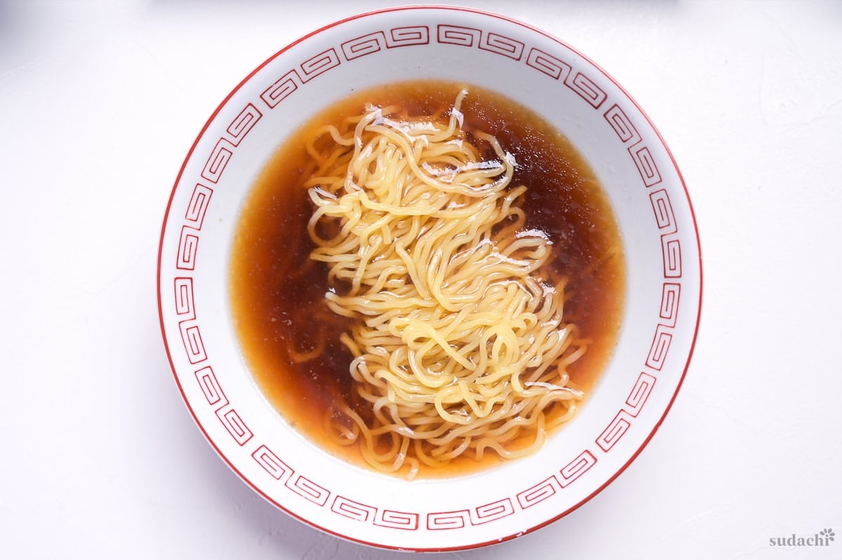 ramen noodles in a soup made with leftover chashu marinade and pork stock in a white ramen bowl with red design on the rim