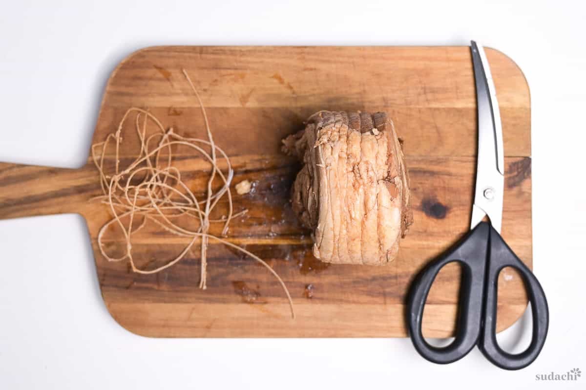butchers twine cut off of the pork on a wooden cutting board