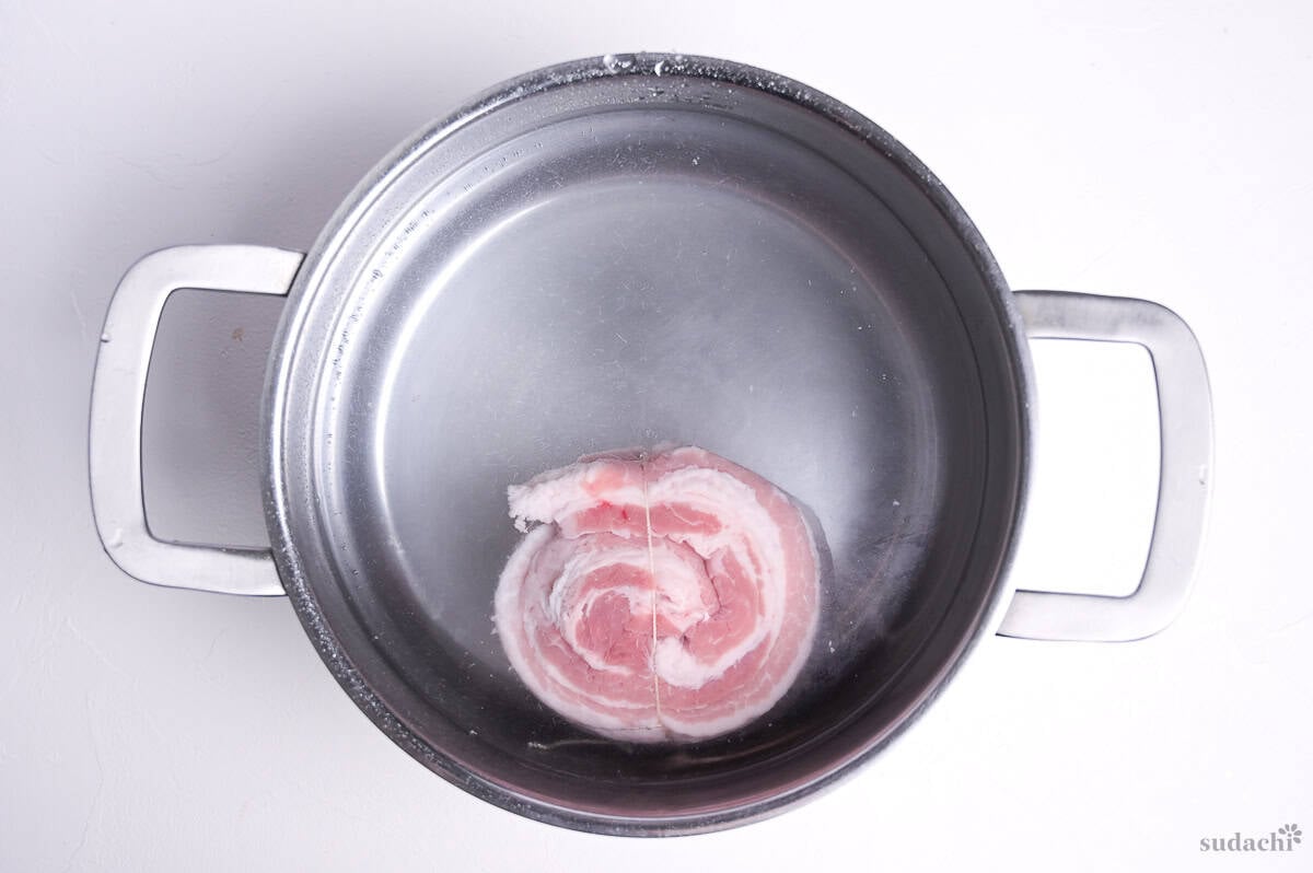 rolled pork belly block in a pot of cold water