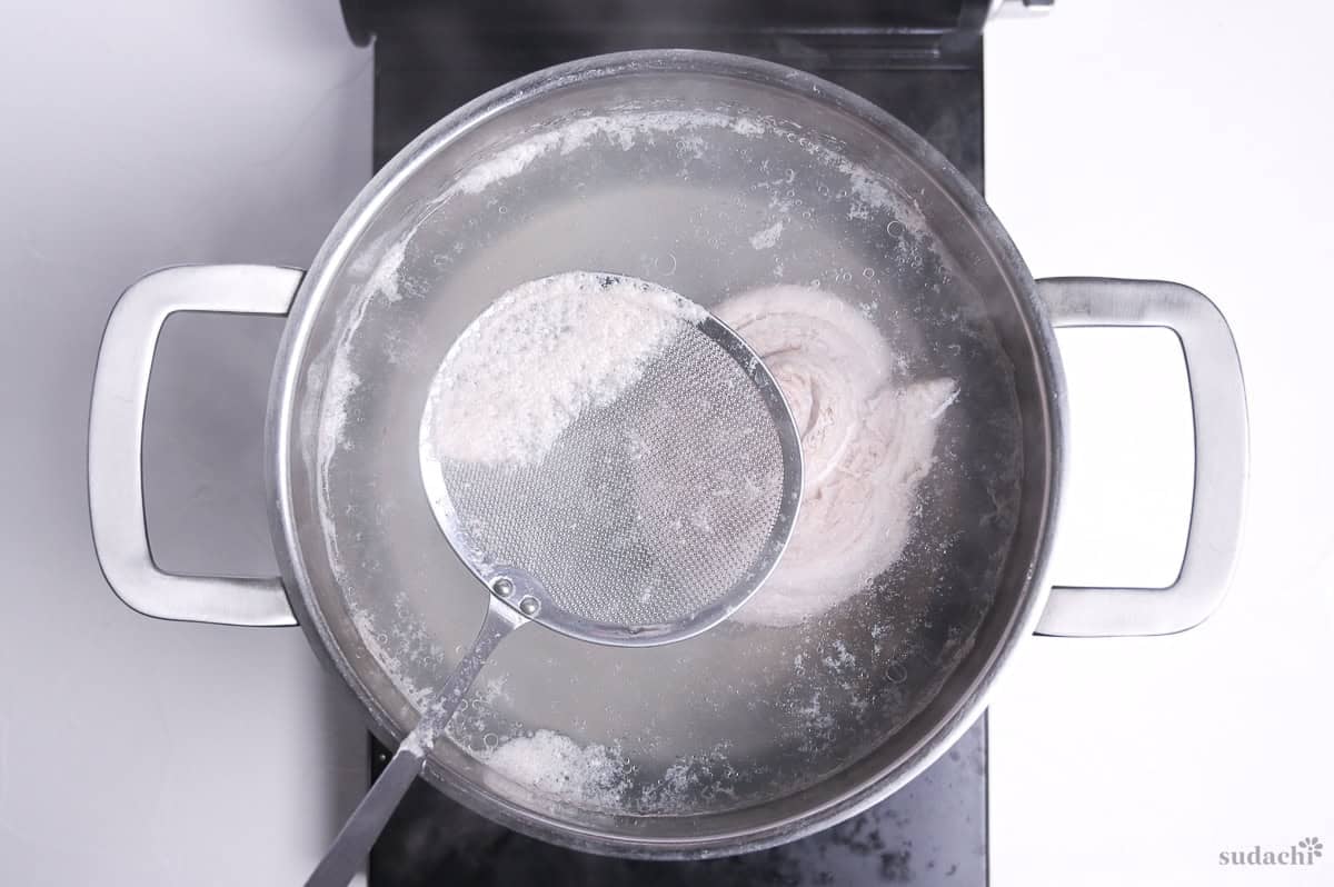 simmering pork belly block with a mesh spoon scooping out the scum
