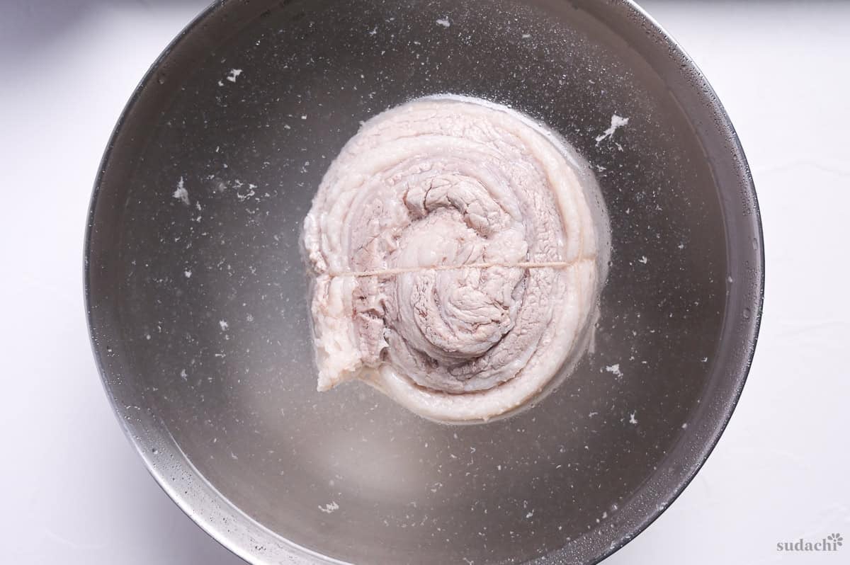 boiled rolled pork belly for chashu in a bowl of cold water