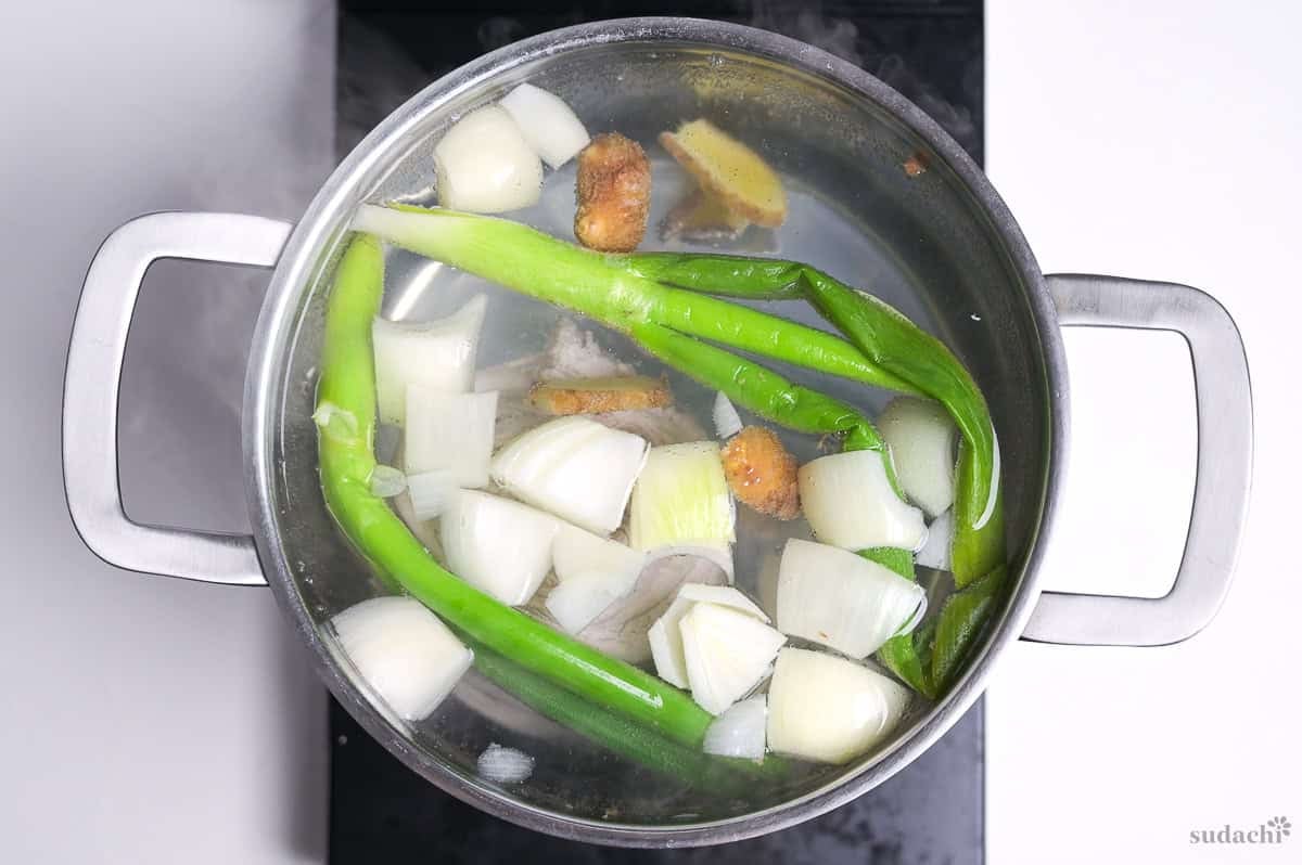 Making stock for chashu with Japanese leek, ginger, garlic, onion and pork belly in a pot of water on the stove top