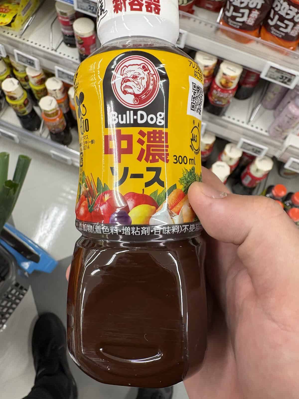 A hand holding a 300ml bottle of Bull-Dog brand Chuno Sauce (中濃ソース), a Japanese medium-thick Worcestershire-style sauce