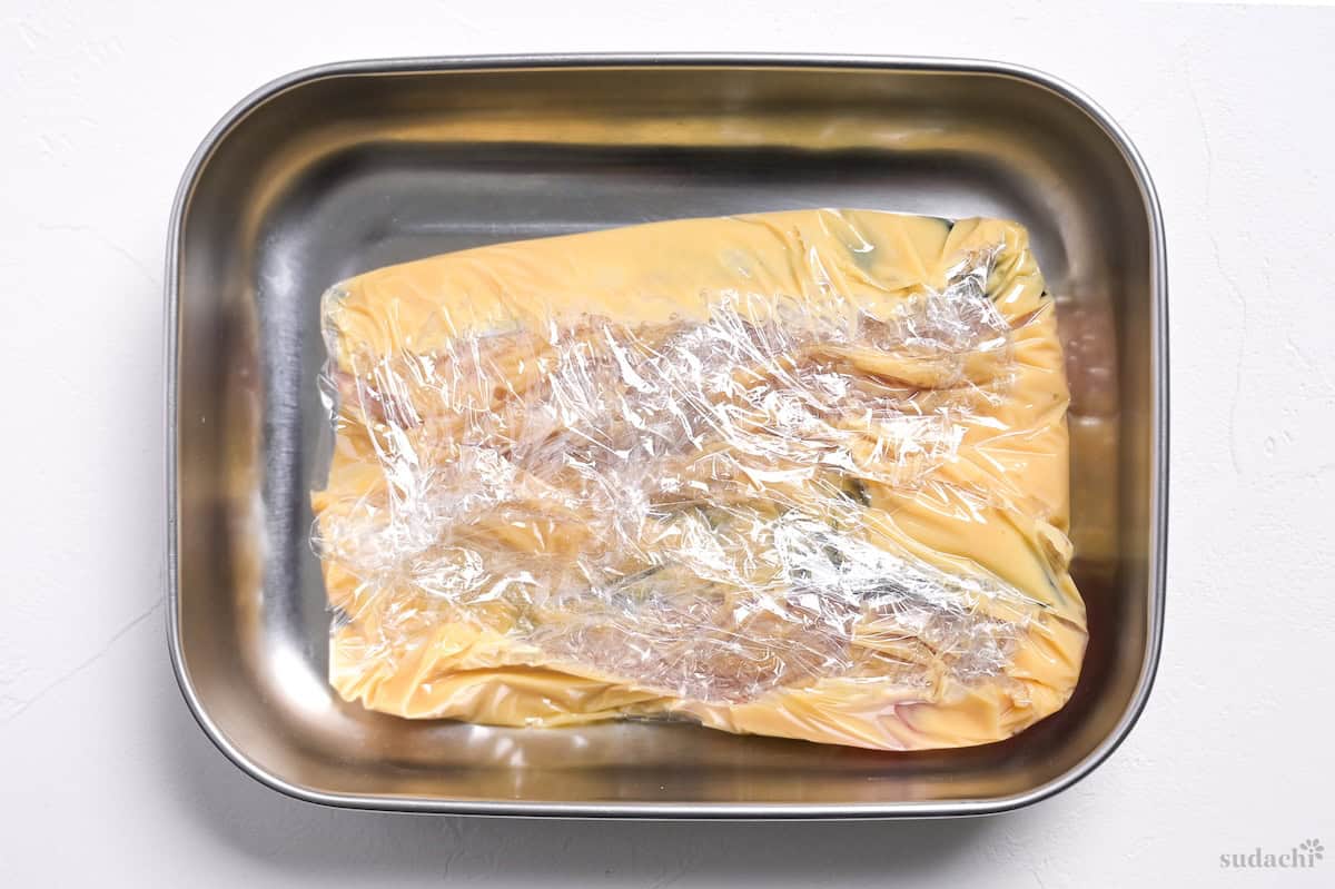 Spanish mackerel fillets coated in white miso marinade wrapped with plastic wrap in a steel container to make saikyo yaki