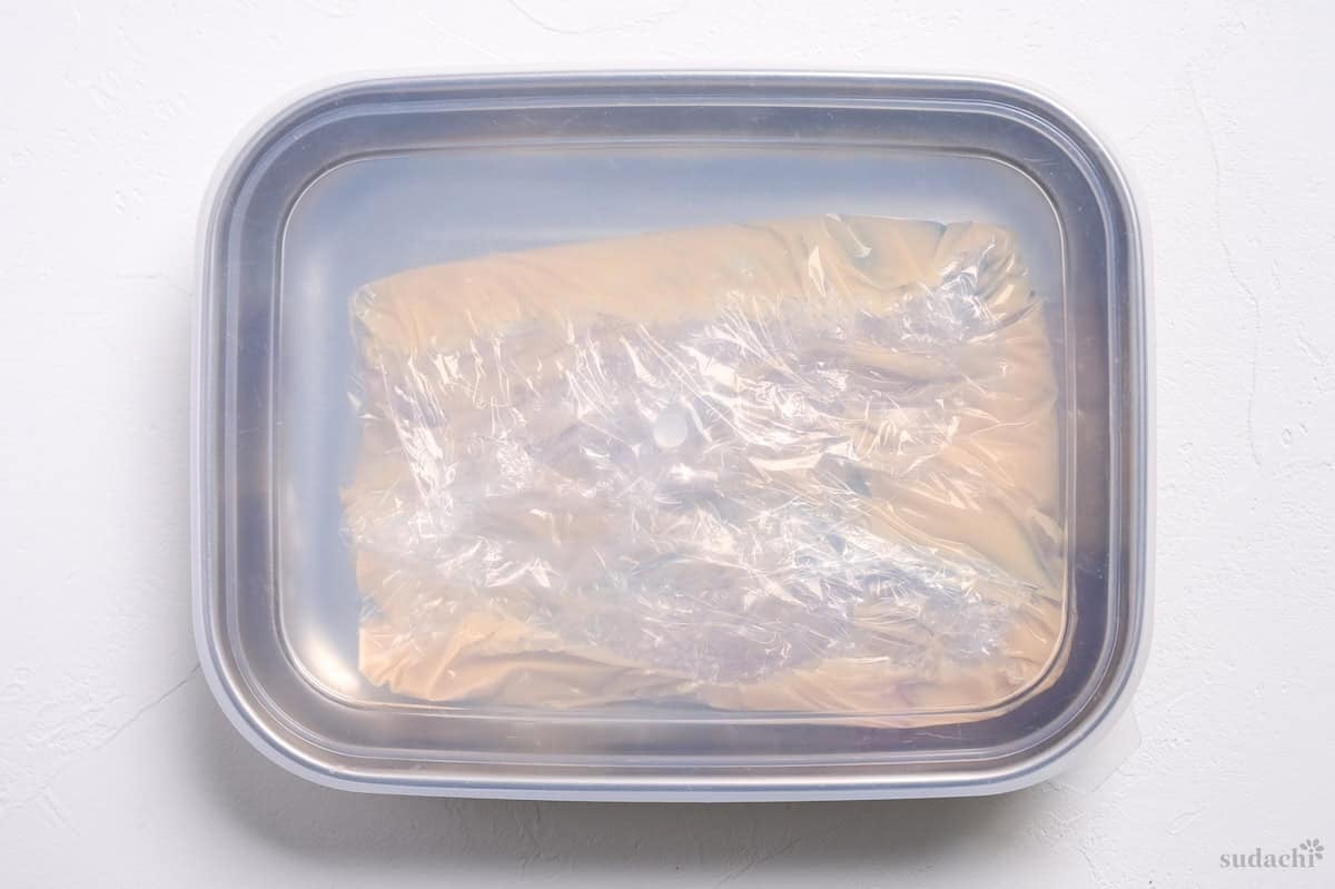 Spanish mackerel fillets coated in white miso marinade wrapped with plastic wrap in a steel container sealed with a lid to make saikyo yaki