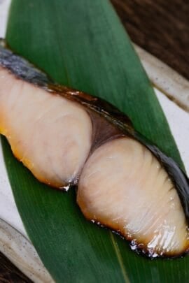 Saikyo Yaki made with Spanish mackerel served over a bamboo leaf on a rectangular cream plate with brown rim
