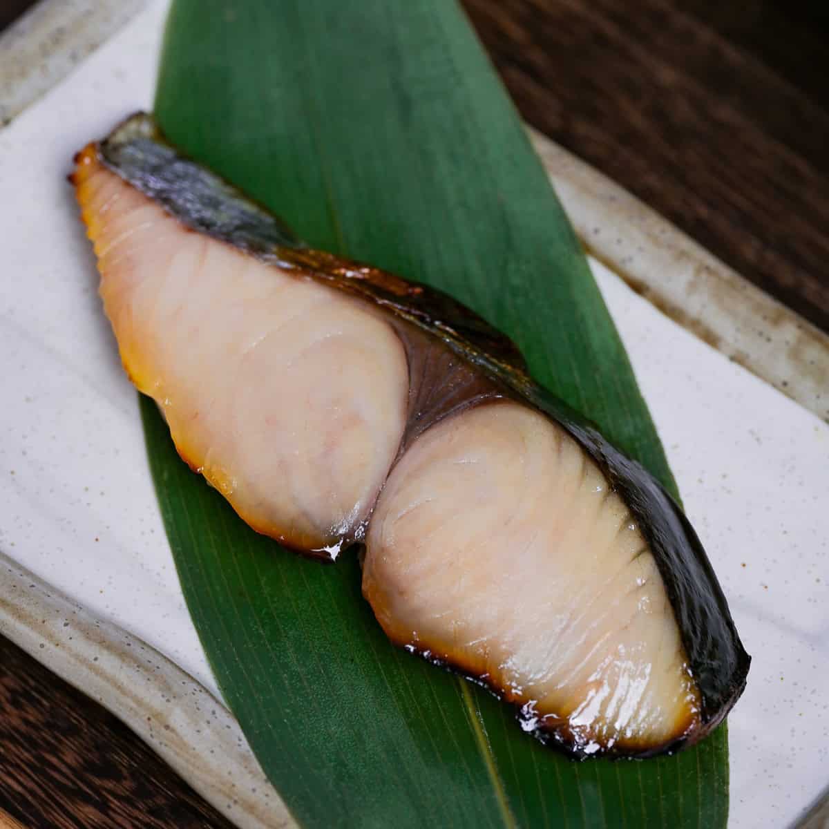 Saikyo Yaki made with Spanish mackerel served over a bamboo leaf on a rectangular cream plate with brown rim