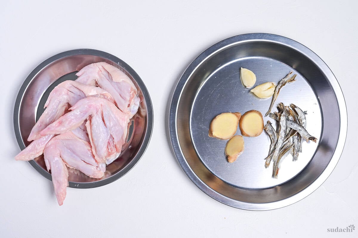 Chicken wings on one plate, and sliced ginger, crushed garlic cloves and niboshi with heads and guts removed on another plate (for making shoyu ramen broth)