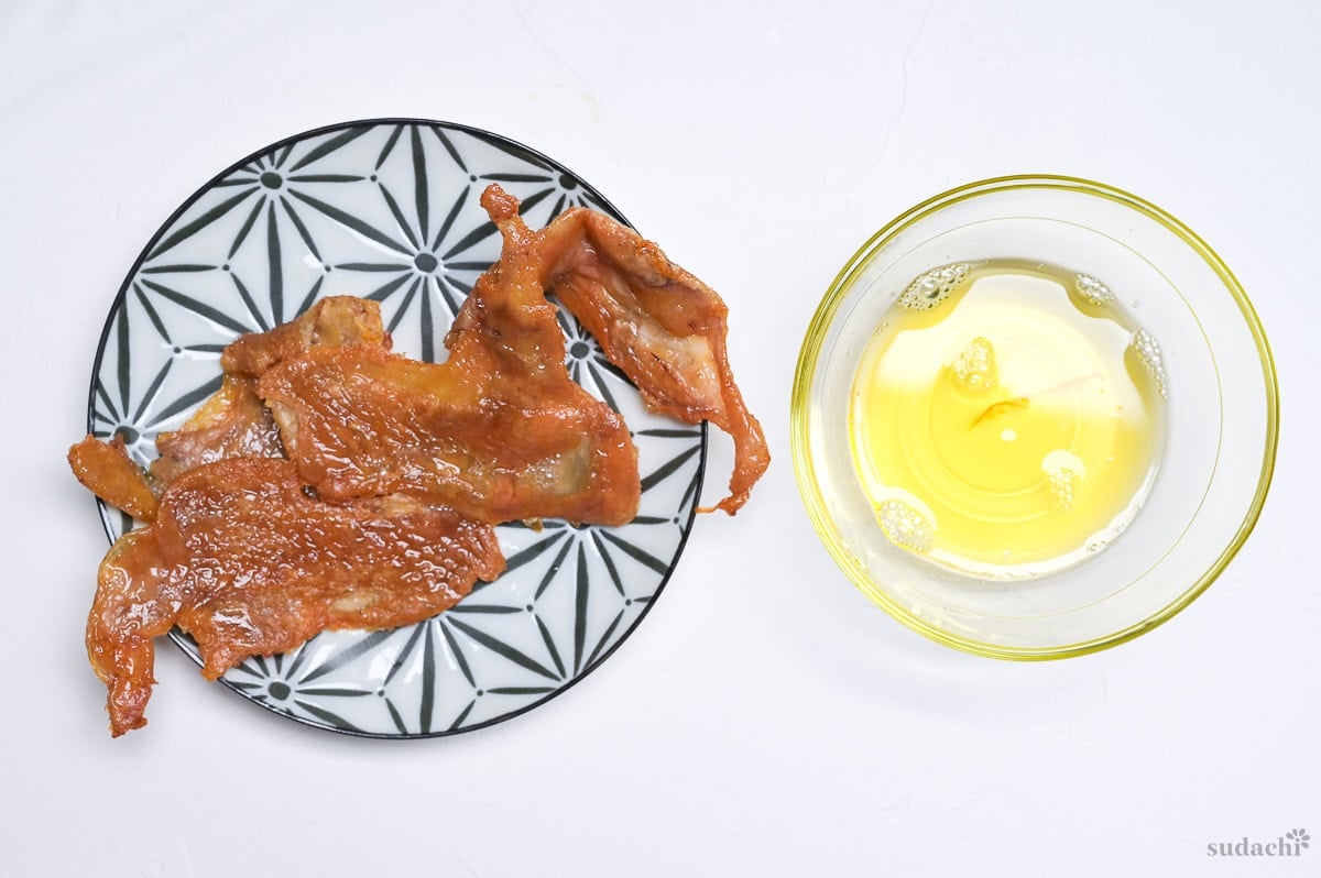 crispy chicken skin on a black and white plate next to rendered chicken fat in a glass bowl