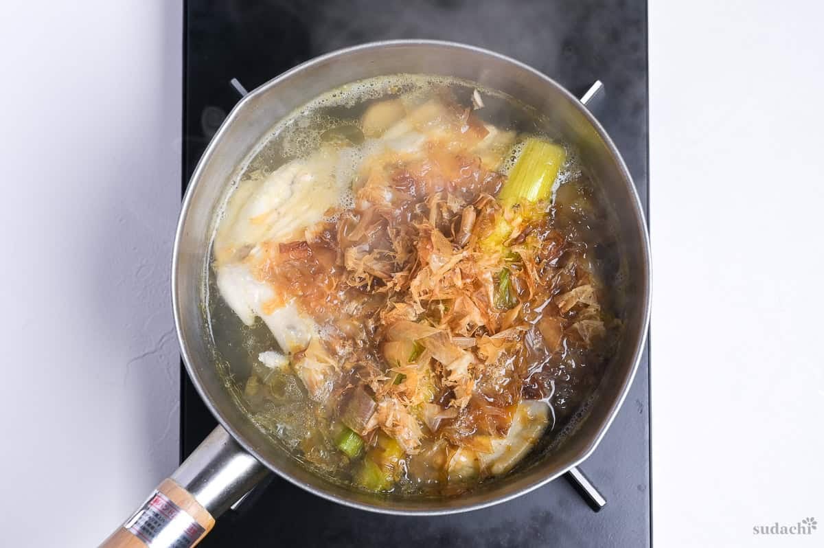 broth for shoyu ramen simmering in a pot on the stove top with bonito flakes dropped in