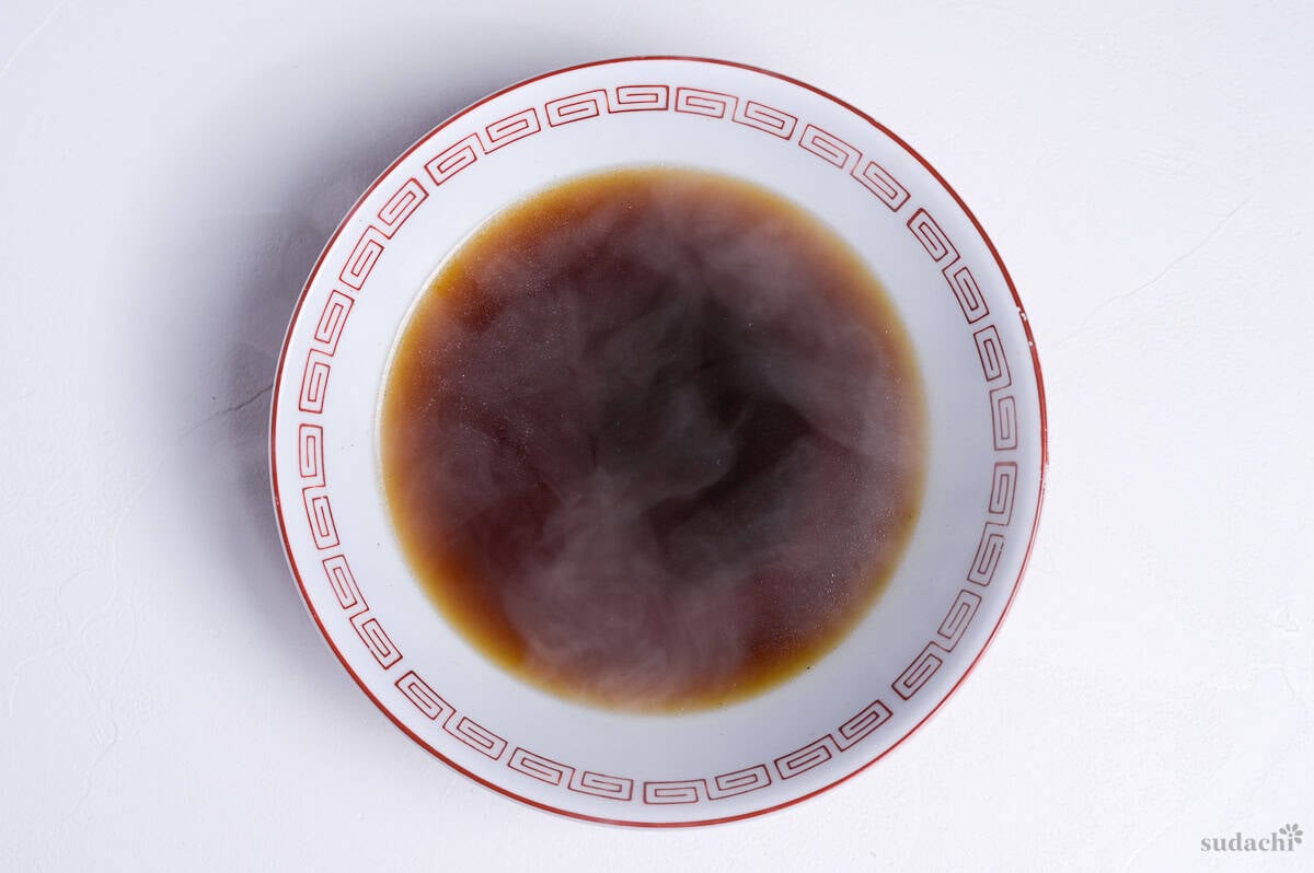 shoyu ramen broth in a white ramen bowl with red design on rim