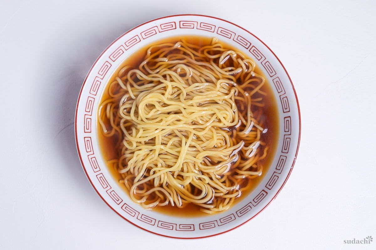 shoyu ramen in a white ramen bowl with red design on rim