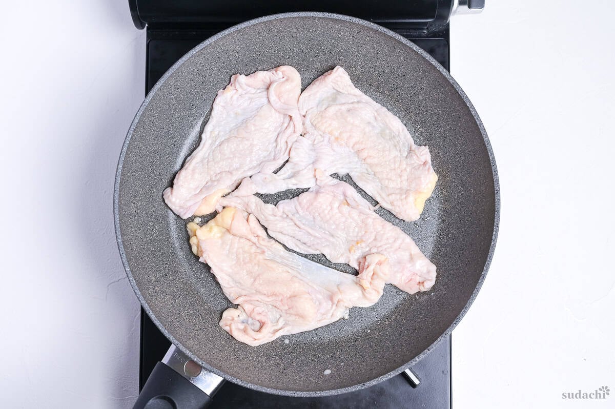 chicken skin spread in a single layer in a frying pan on the stove top