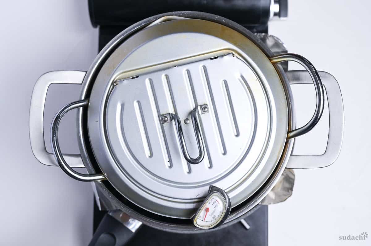 a heavy pot of water weighing down chicken skin topped with foil in a frying pan